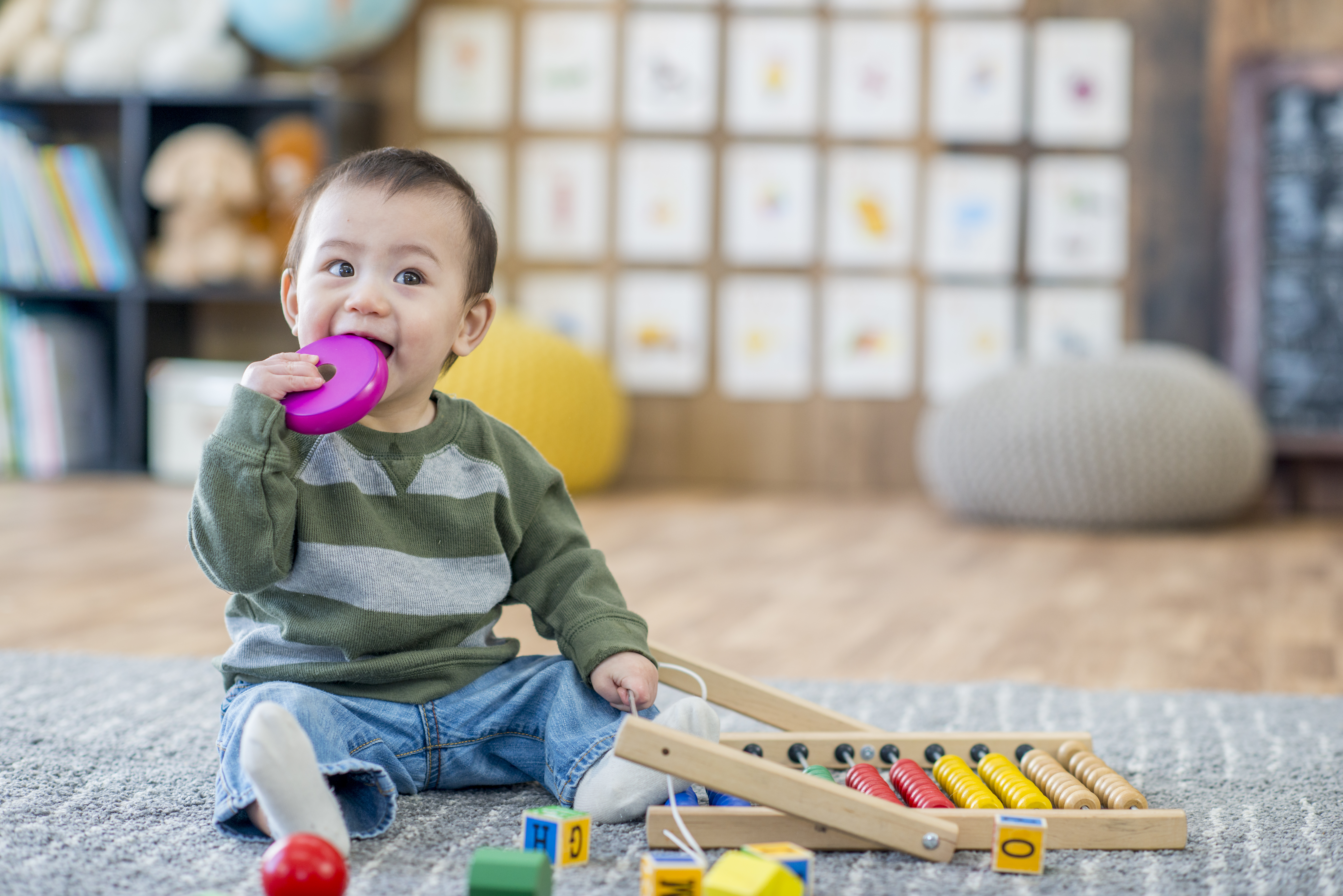 Asian baby sitting with toy in mouth