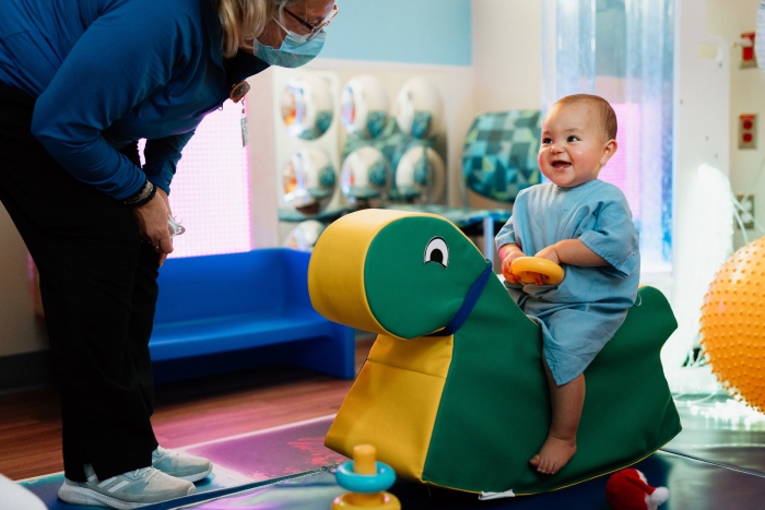 infant rocking on play horse in the sensory room at Dayton Children's