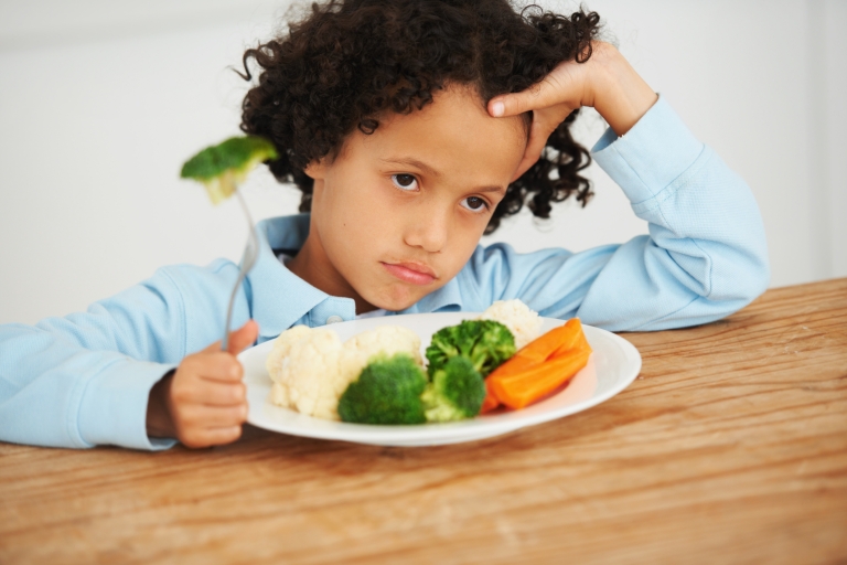 boy at the table with broccoli on a fork with a disgusted look on his face