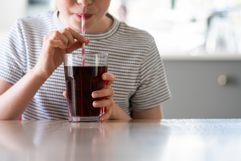 girl drinking a dark colored soda with a red and white striped straw