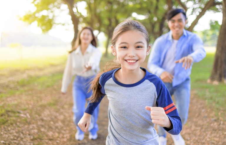 young girl running outdoors with parents behind her