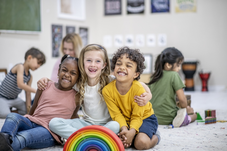group of diverse children sitting and smiling with a rainbow toy